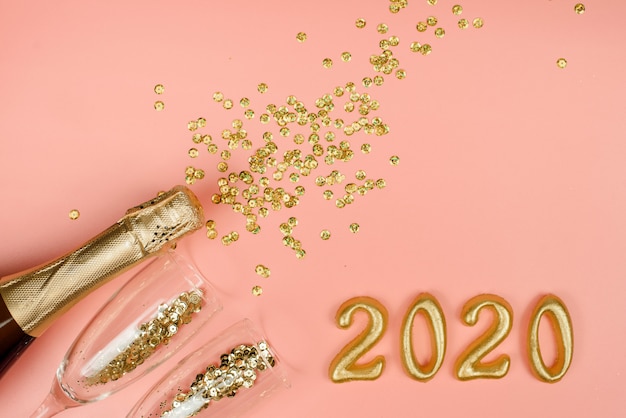 Flasche Champagner, klare Gläser mit goldenen Konfetti und goldenen Zahlen auf einem rosa Pastell