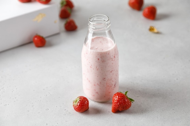 Flasche Erdbeerjoghurt oder Milch auf grauem Tisch und Beeren im Hintergrund