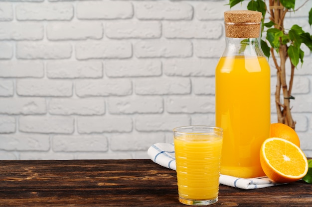 Flasche frischer Orangensaft auf Holztisch gegen weißen Backsteinmauerhintergrund