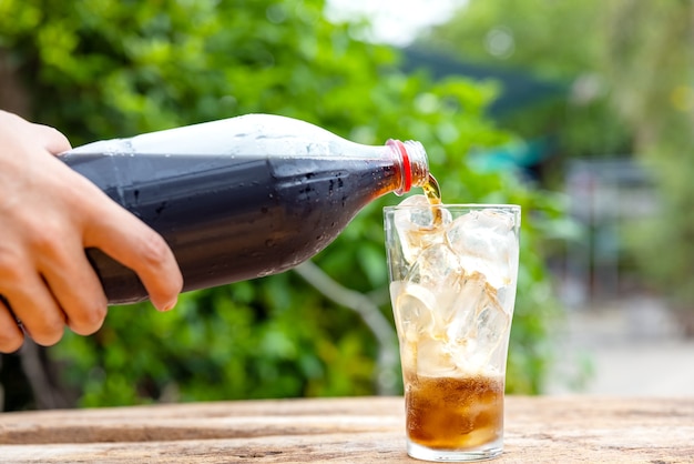 Flasche gießt Getränk im Glas auf Holztisch im Garten