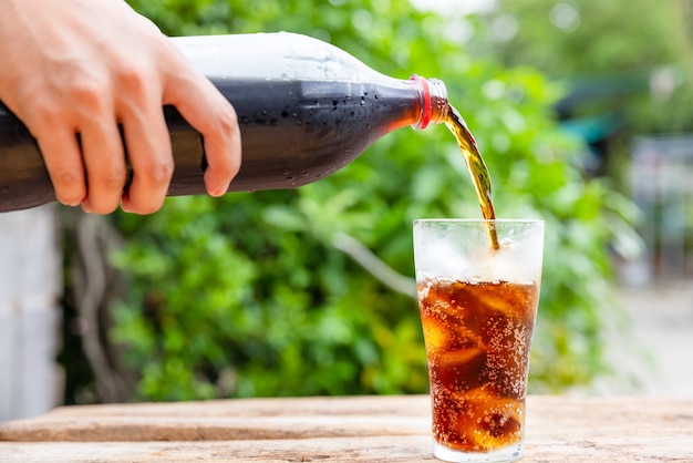 Flasche gießt Getränk im Glas auf Holztisch im Garten