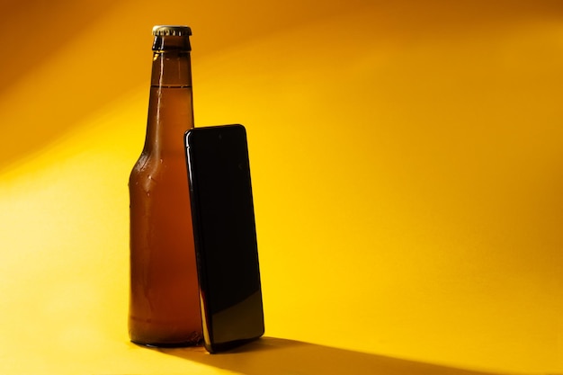 Flasche kaltes Bier geschlossen auf gelbem Hintergrund mit Handyschatten