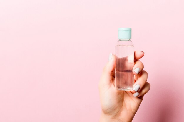 Flasche kosmetisches Produkt in einer weiblichen Hand am rosa Hintergrund