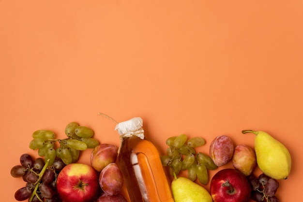 Flasche mit Apfelwein oder Essig mit rohen Herbstfrüchten auf orange Hintergrund-Draufsicht-Kopienraum