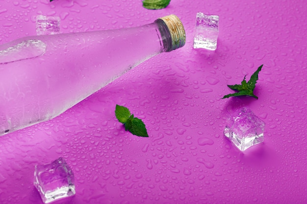Flasche mit einem Eisgetränk in Kondensationstropfen, Eiswürfeln und Minzblättern