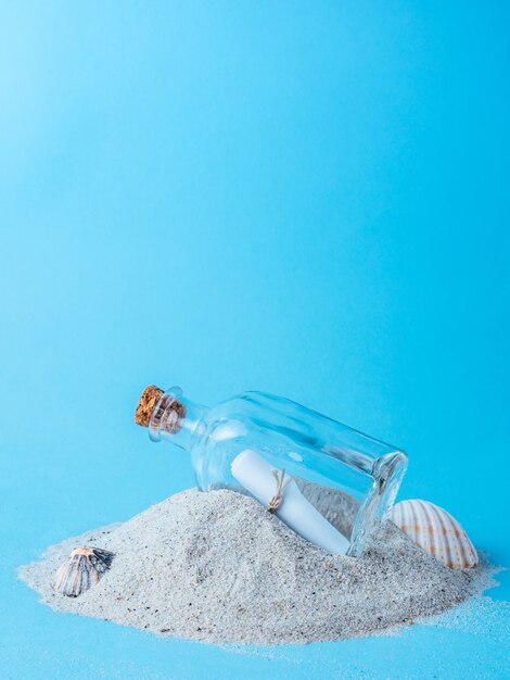 Flasche mit einer Nachricht auf Sand mit blauem Hintergrund