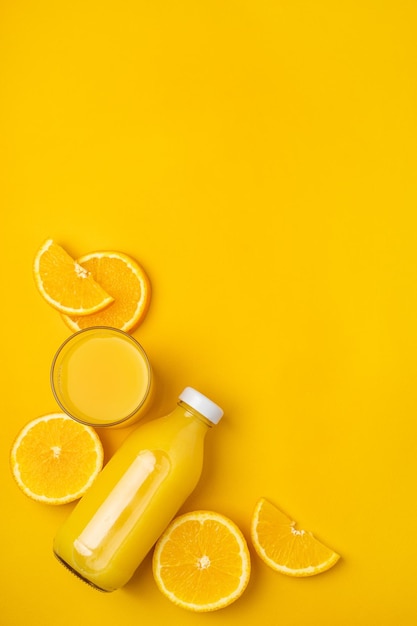 Flasche mit Saft und Orangen auf gelbem Hintergrund