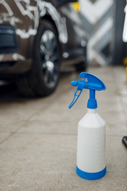 Flasche mit spritzpistole, auto mit schutzfolie, niemand. anbringen einer beschichtung, die den lack des autos vor kratzern schützt. neues fahrzeug in garage, autotuning