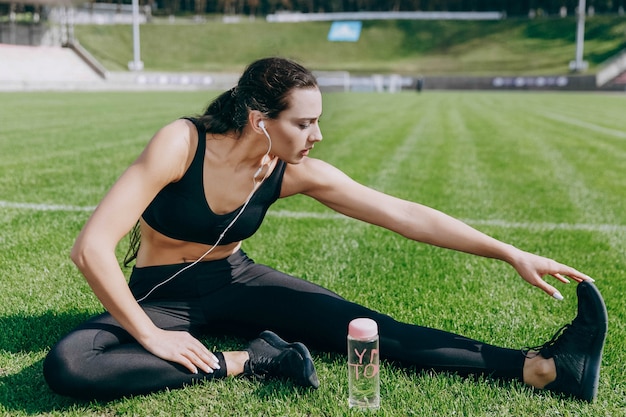 Flasche mit Wasser steht vor der jungen Frau, während sie sich im Stadion aufwärmt und Musik hört