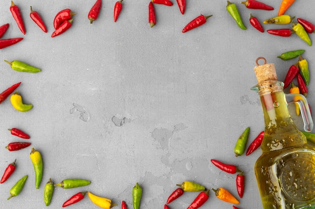 Flasche Olivenöl und Chilischoten auf grauem Hintergrund