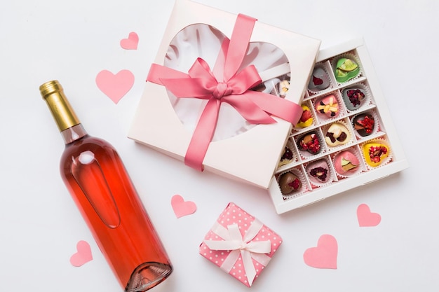 Foto flasche rotwein auf farbigem hintergrund für valentinstag mit geschenk und schokolade herzform mit geschenkbox mit schokolade top-view mit kopierplatz