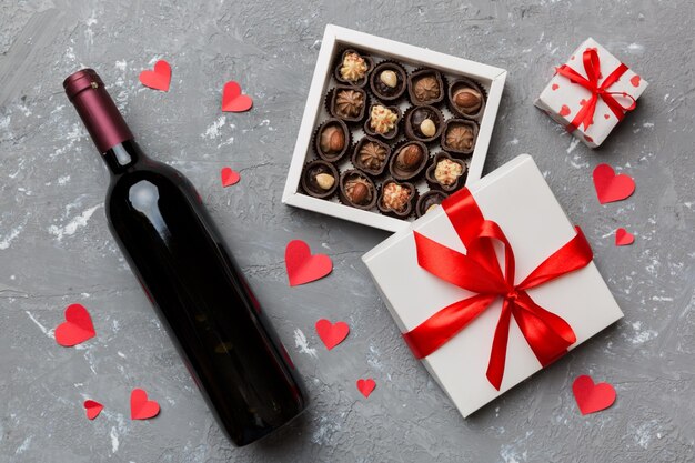 Flasche Rotwein auf farbigem Hintergrund zum Valentinstag mit Geschenk und Schokolade Herzförmig mit Geschenkbox Pralinen Draufsicht mit Kopierraum