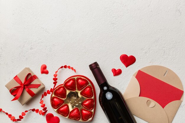 Flasche Rotwein auf farbigem Hintergrund zum Valentinstag mit Geschenkboxumschlag und Schokolade Herzförmig mit Geschenkbox Pralinen Draufsicht mit Kopierraum