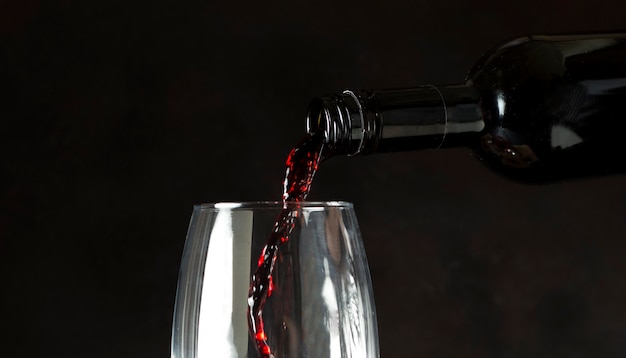 Flasche Rotwein in Glas auf schwarzem Hintergrund gießen
