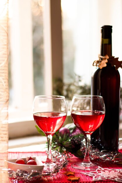 Foto flasche rotwein und zwei volle gläser in der nähe des lichtfensters, festliche neujahrsportion