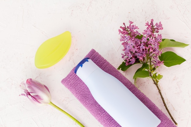 Flasche Shampoo, Handtuch, Seife, Tulpe und lila Blüten auf strukturiertem Hintergrund