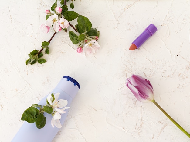 Flasche Shampoo, Lippenstift, Tulpe und Blumen eines Apfelbaums auf strukturiertem Hintergrund. Damenaccessoires für Badevorgänge. Ansicht von oben.