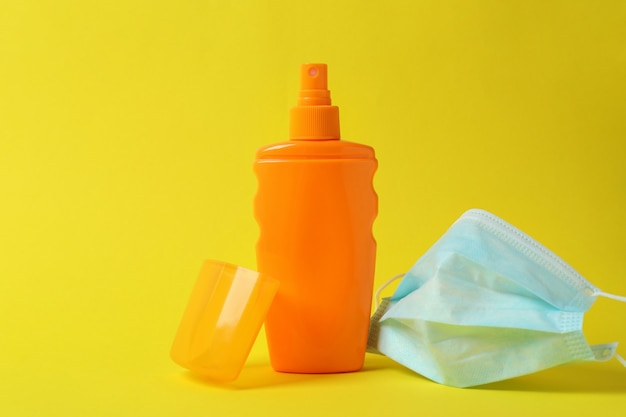 Flasche Sonnenschutzmittel und medizinische Maske auf gelbem lokalisiertem Hintergrund