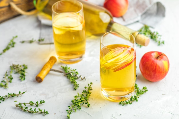 Flasche und Gläser hausgemachten Bio-Apfelweins mit frischen Äpfeln in einer Tischplatte aus hellem Beton mit geringer Schärfentiefe