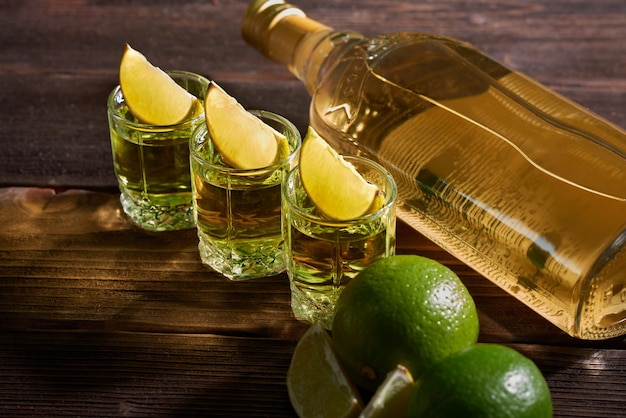 Flasche und Gläser Tequila mit Kalk auf einem Holztisch Traditionelles mexikanisches alkoholisches Getränk