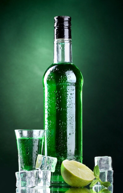 Flasche und Glas Absinth mit Kalk und Eis auf grünem Hintergrund