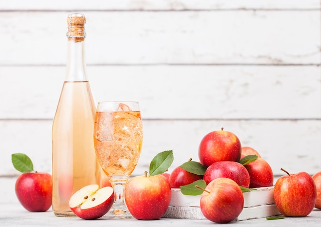 Flasche und Glas hausgemachter Bio-Apfelwein mit frischen Äpfeln im Karton auf Holzhintergrund Glas mit Eiswürfeln