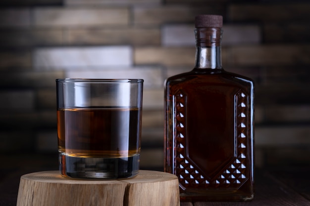 Flasche und Glas mit Alkohol auf einem Holzständer gegen eine Mauer