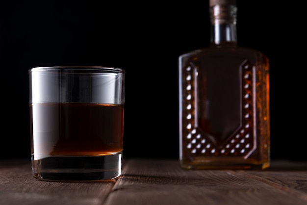Flasche und Glas mit Alkohol auf einem Holztisch im Dunkeln