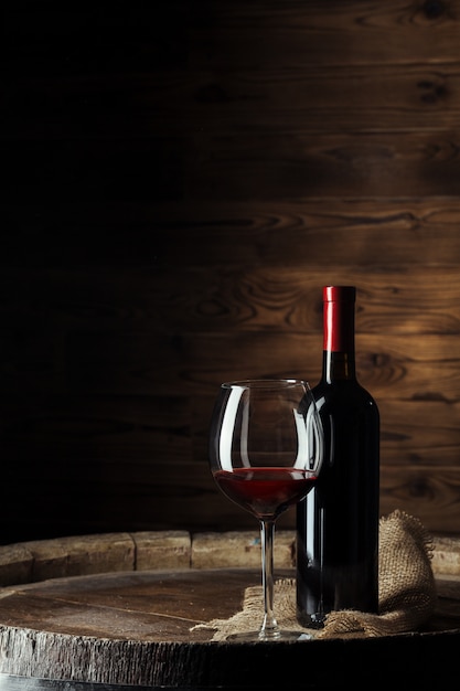 Foto flasche und glas rotwein auf hölzernem fass schossen mit dunklem hölzernem hintergrund