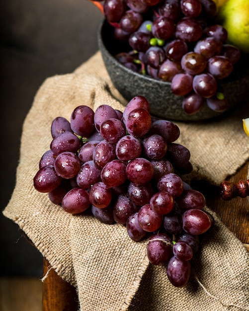 Flasche und Glas Rotwein, Traube und Kork auf Stuhl. Melone, Stück Melone. Rosa Traube, Birne. Stillleben des Essens. Dunkle Food-Fotografie. Herbstkonzept. Alkohol, Weinbau.