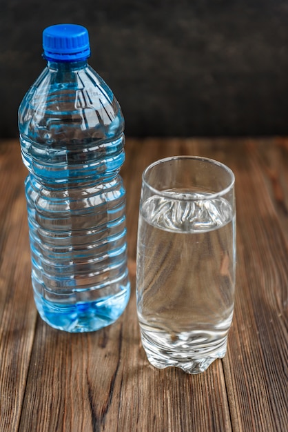 Flasche und Glas Wasser auf Holzfläche.