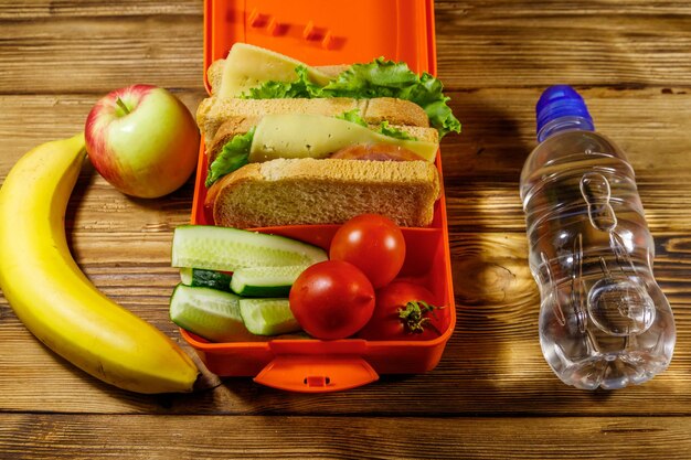 Flasche Wasser Apfel Banane und Brotdose mit Sandwiches und frischem Gemüse auf einem Holztisch