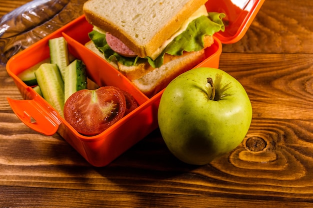 Flasche Wasser grüner Apfel und Brotdose mit Sandwich-Gurken und Tomaten auf Holztisch