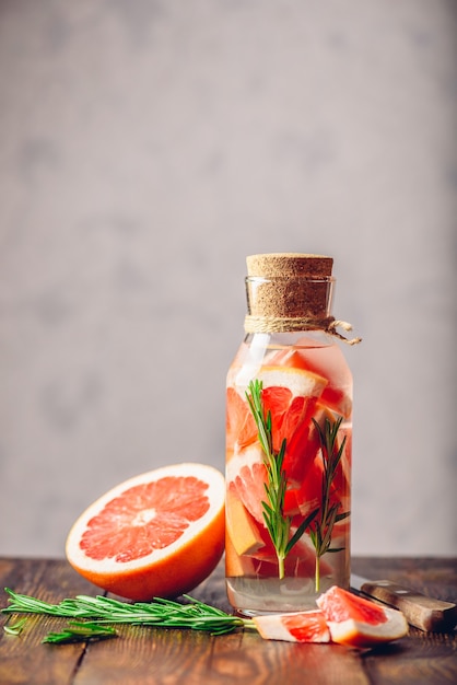 Flasche Wasser mit geschnittener Grapefruit und frischen Rosmarinquellen. Zutaten und Messer auf Holztisch