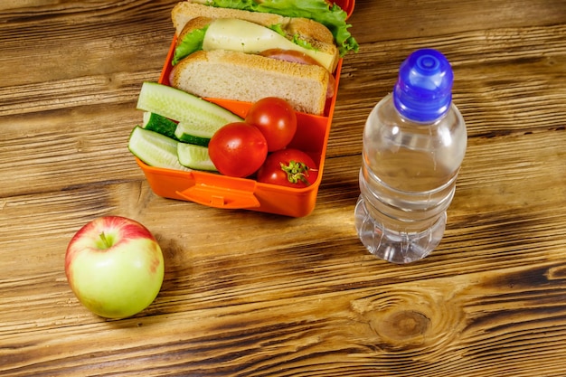 Flasche Wasserapfel und Lunchbox mit Sandwiches und frischem Gemüse auf einem Holztisch