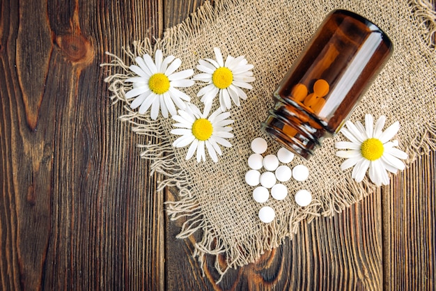 Flasche weiße Kräuterpillen und Kamillenblüten auf dunklem Holz, homöopathische Medizin.