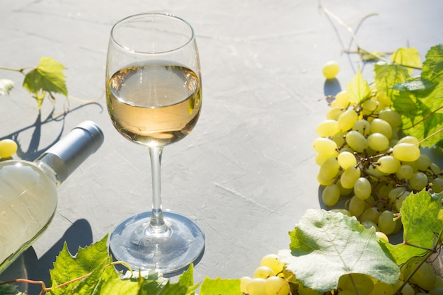 Foto flasche weißwein mit weinglas, reife traube auf konkreter grauer tabelle.