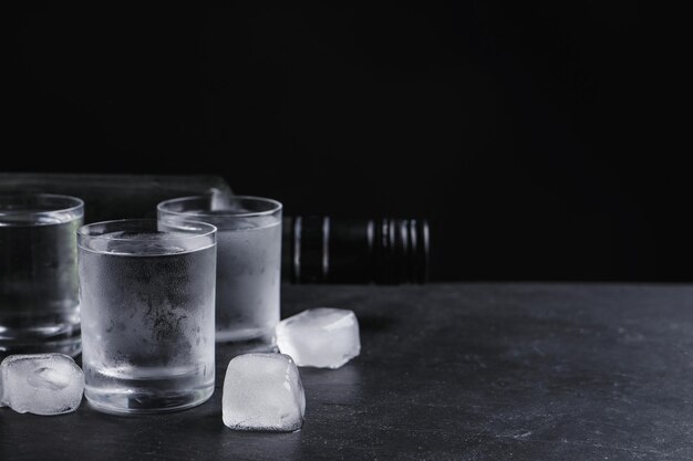 Flasche Wodka und Schnapsgläser mit Eis auf dem Tisch vor schwarzem Hintergrund Platz für Text