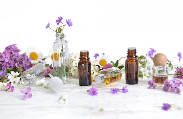 Flaschen ätherisches Öl und bunte Blütenblätter von Blumen auf weißem Tisch