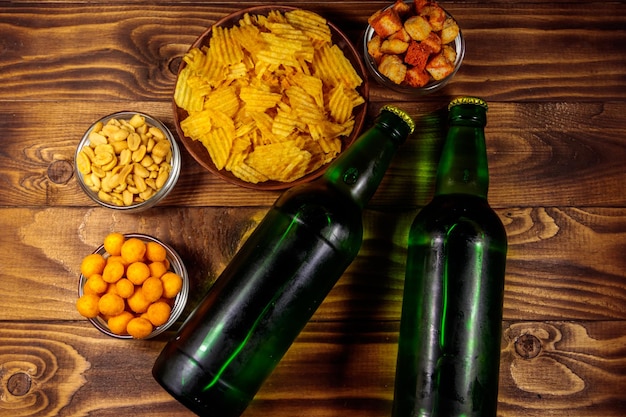 Flaschen Bier und verschiedene Snacks für Bier auf Holztisch. Ansicht von oben