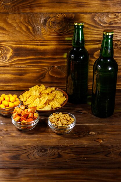 Flaschen Bier und verschiedene Snacks für Bier auf Holztisch