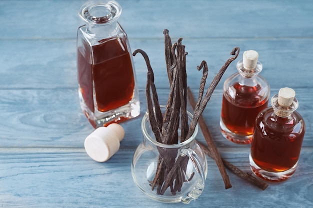 Flaschen mit aromatischem Extrakt und trockenen Vanilleschoten im Krug auf dem Tisch