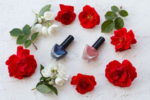 Flaschen mit Nagellack auf weißem Hintergrund mit Knospen von Rosenblüten. Frauenkosmetik und Accessoires. Draufsicht.