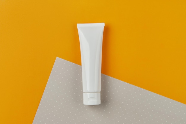 Flasco de tubo branco em branco com creme de loção ou limpeza em fundo laranja conceito de bem-estar de cuidados com a pele facial