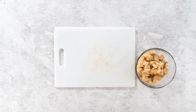 Flat lay cortando pão amanhecido com uma faca de pão em uma tábua branca para fazer croutons