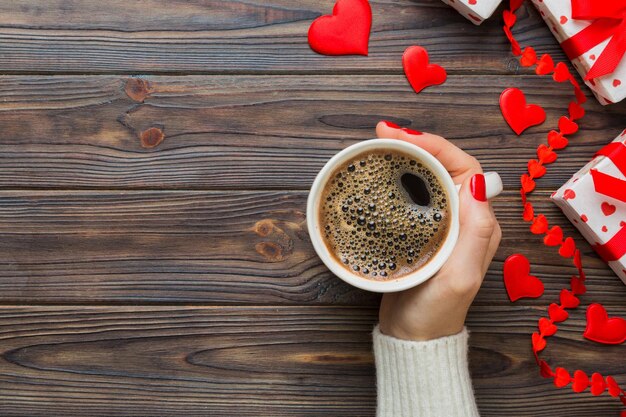 Flat lay de xícara em forma de coração de café preto nas mãos de mulheres em fundo colorido com cópia de espaço top view dia de São Valentim e conceito de feriado