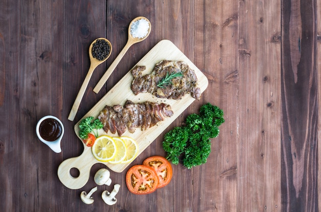 Flat lay filete de ternera a la plancha sobre tabla de cortar de madera y verduras