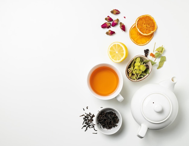 Flat lay uma xícara de chá preto, frutas e chá de ervas, com limão e bule de chá em um fundo branco. O conceito de uma bebida saudável. Vista superior e copie o espaço.