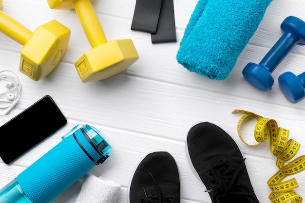 Flat lay vista superior equipos deportivos, zapatillas de deporte y teléfono inteligente sobre fondo blanco de madera