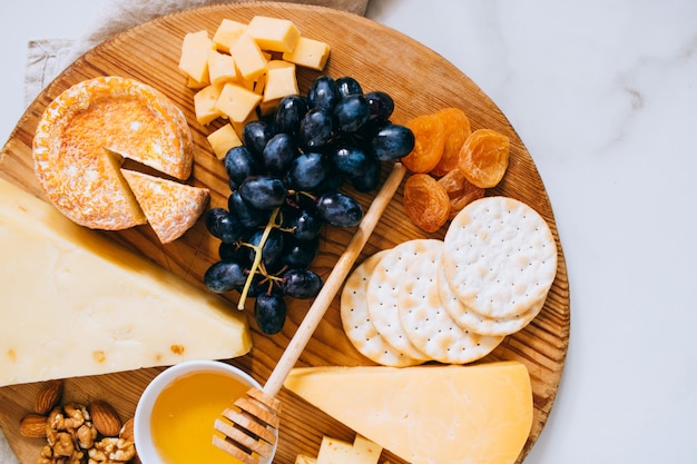 Flat leigos com vários tipos de queijo, uvas, nozes, mel e bolacha na placa de madeira em mármore